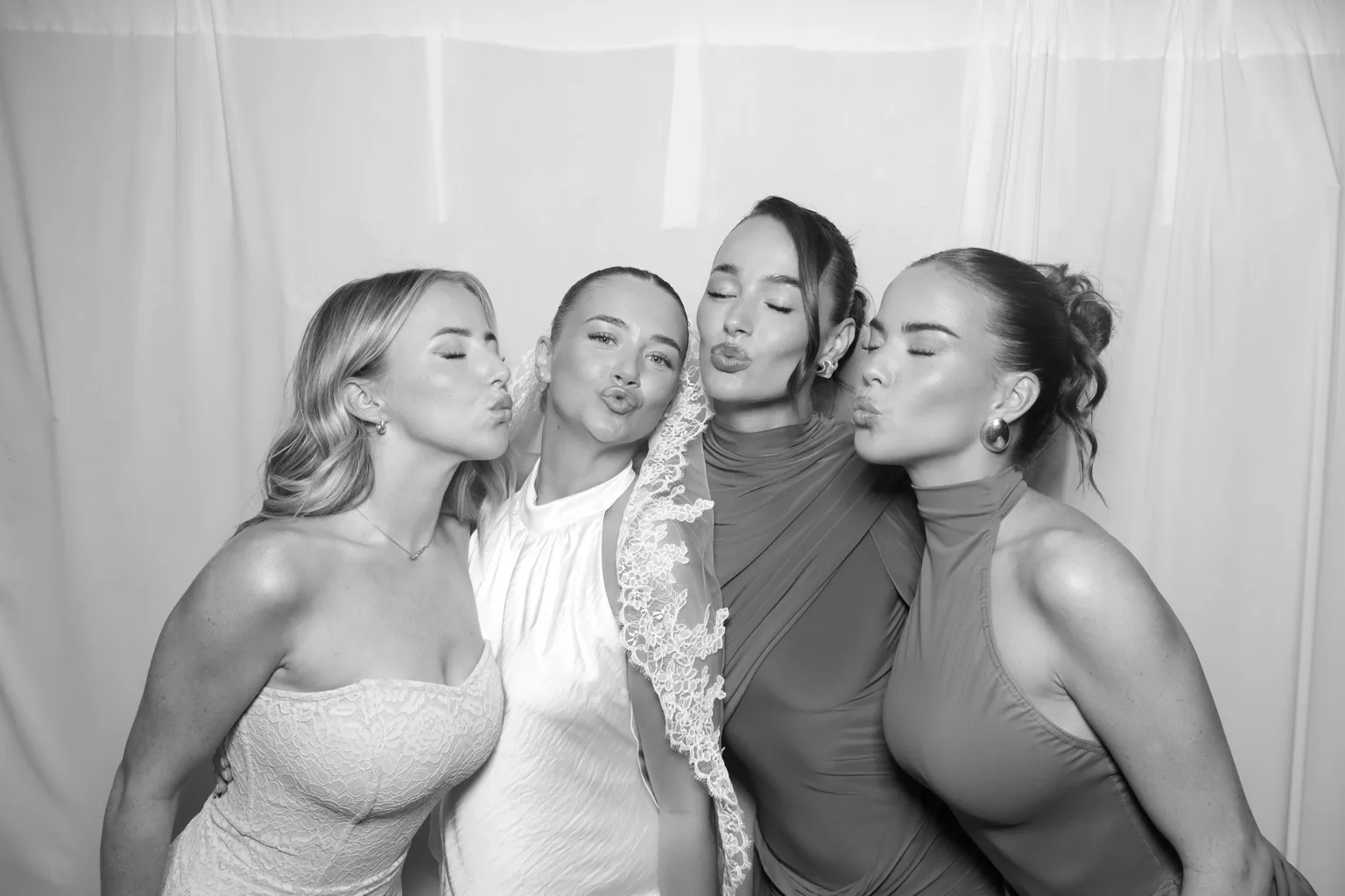 Four guests posing for a Selfie Glam Booth black-and-white portrait against white drapes