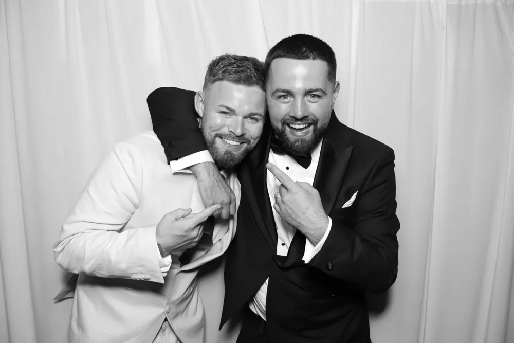 Two friends smiling together against white drapes